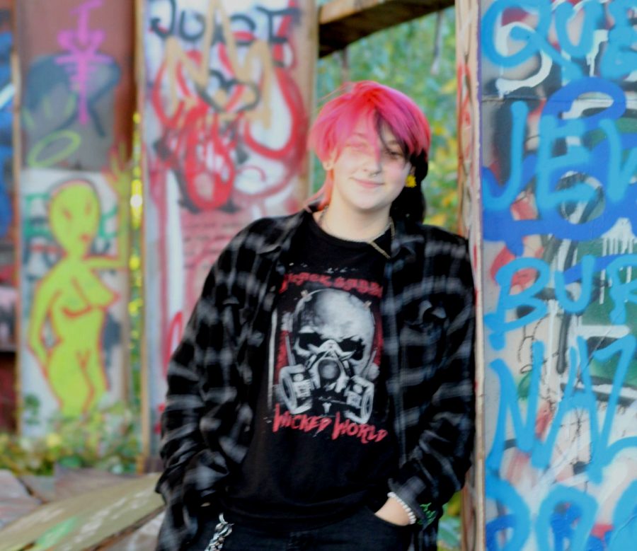 Man with split dyed hair leaning on heavily gratified pillar. He is wearing black jeans, a Black Sabbath Shirt and a black and grey flannel.