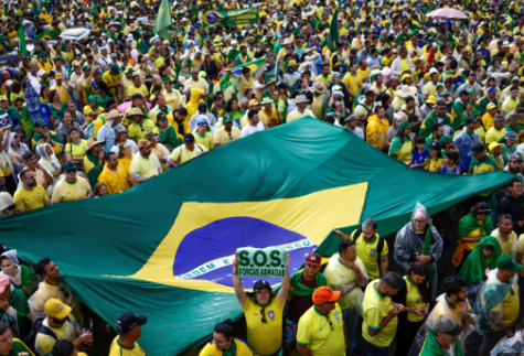 Crowd with hundreds of people holding signs, Brazilian flags, and wearing Brazilian colors. in the middle there is a giant brazilian flag.