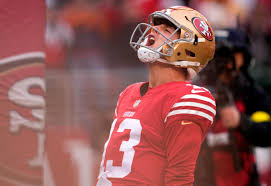 49ers Quarterback Brock Purdy in the foreground yelling in passion into the air.