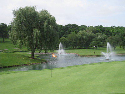 Golf Course hole that has a water fountian surrounded by trees.