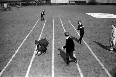 The Beatles racing each other on a grass field track after sneaking away from their duties.