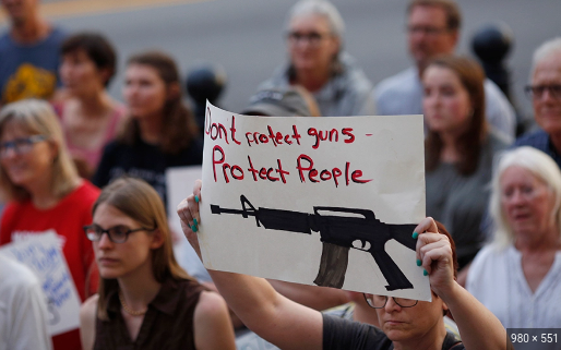 Crowd of people in the background with a sign in the foreground that says dont protect guns protect people.