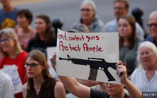 Crowd of people in the background with a sign in the foreground that says don't protect guns protect people.